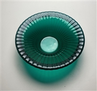 A top-down view of a teal fused glass bowl on a light grey background. It has a texture of many small ridges radiating outwards from the flat circular center.