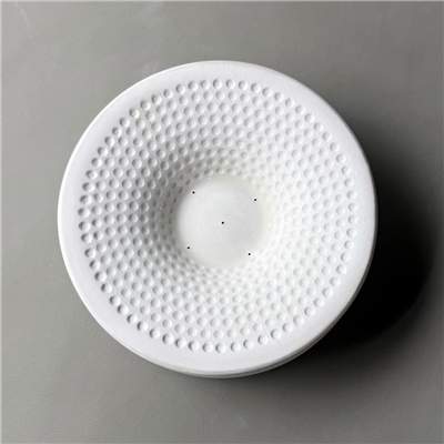 A circular white ceramic mold for fusing glass on a grey background. There is a small flat circle carved in the center. There are smaller circular dots carved around it, rising up in concentric rings around the rim of the mold.
