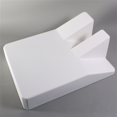 A large rectangular white ceramic mold for fusing glass on a grey background. One end angles downwards. On the edge of the angled end is a  U-shaped structure, with the arms of the U angled above the level of the other side of the rectangle.