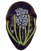 A fused glass mask in the shape of a human face. The base glass is a dark purple, and instead of facial features it has been decorated with a large flower made of several thin green stems and small lilac beads of glass as the flower.