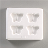 A square white ceramic mold for fusing hot glass on a grey background. Four identical small and simple butterflies have been carved into it with equal space between them. The mold says LF17 at the bottom.