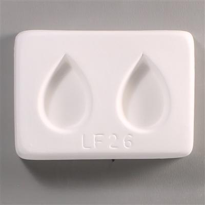 A rectangular white ceramic mold for fusing hot glass on a grey background. Two separate but identical teardrop shapes have been carved into it. LF26 is carved onto the mold beneath them.