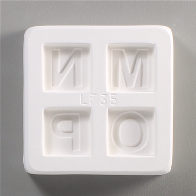 A square white ceramic mold for fusing hot glass on a grey background. Four separate but identically sized squares have been carved into it with equal space between them. Each square has one of the letters M, N, O, or P carved in block print in it.