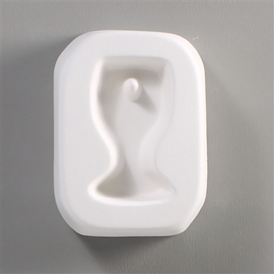 A rectangular white ceramic mold for fusing hot glass on a grey background. A simple wine glass shape has been carved into it. There is a post towards the top of the glass allowing for the resulting piece to be strung as jewelry.