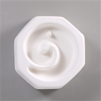 An octagonal, white ceramic mold for fusing hot glass on a grey background. A simple counterclockwise spiral has been carved into it. There is a small post at the top of the spiral so the finished piece can be strung as jewelry.