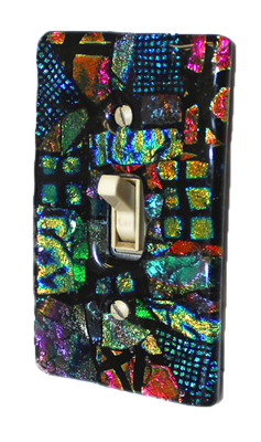 A light switch with a fused glass switch plate on a transparent background. The switch plate has a black background and is filled with various colors and shapes of reflective dichroic glass.
