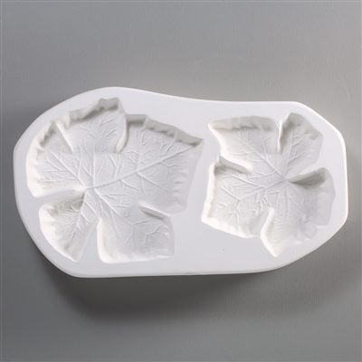 A roughly rectangular, white ceramic mold for fusing hot glass on a grey background. Two detailed flat grape leaves have been carved into it. The leaf on the left is slightly larger.