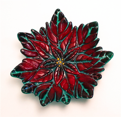 A lightly cupped fused glass poinsettia flower on a white background. The flower is mostly a deep red, with the detail lines filled a dark green and a few bright yellow circles at the very center.