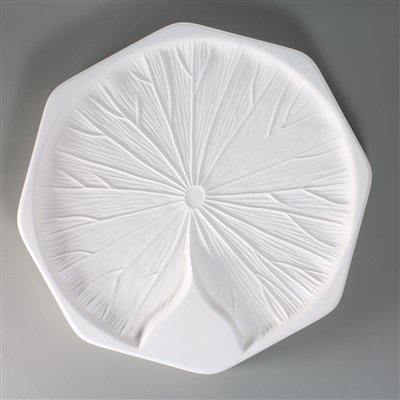 An octagonal, white ceramic mold for fusing hot glass on a grey background. A large detailed flat lily pad has been carved into it. The lily pad has a triangular notch at the bottom, and the veins on the pad are prominent.