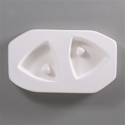 A roughly rectangular, white ceramic mold for fusing hot glass on a grey background. Two triangles with rounded sides have been carved into it. Each triangle has a smaller raised triangle towards the top where a string can pass through after firing.