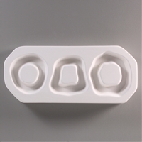 A rectangular, white ceramic mold for fusing hot glass on a grey background. Three wavy ring shapes have been carved into it. The leftmost ring is circular, the middle is more trapezoidal, and the rightmost is a larger, wavier circle.