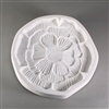 A circular, white ceramic mold for fusing hot glass on a grey background. A small, intricately detailed flat poppy flower has been carved into it. The flower takes up most of the mold, but there is a small border of empty space around it.