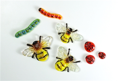 An assortment of fused glass bugs on a white background. There are three yellow and black bees with transparent wings, three red ladybugs with black dots, and two caterpillars, one green and blue and one orange and yellow.