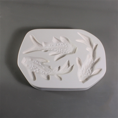 A roughly oval, white ceramic mold for fusing hot glass on a grey background. A top-down view of three separate koi fish has been carved into it. Each fish is similarly sized, but in slightly different swimming positions.