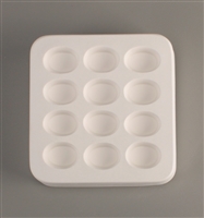 A square white ceramic mold for fusing hot glass on a grey background. Twelve identical ovals have been carved into it with equal space between them.