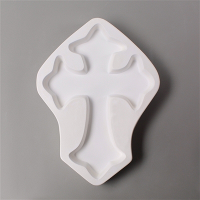 A cross-shaped white ceramic mold for fusing hot glass on a grey background. A large, simple cross has been carved into it.