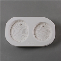 A rectangular white ceramic mold for fusing hot glass on a grey background. Two flat circular log slices have been carved into it, each showing age ring details. The left slice is slightly larger. Each slice has a post at the top to hang from.