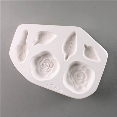 A roughly oval-shaped white ceramic mold for fusing hot glass on a grey background. Two flat rose flowers, one closed rose bud, and three slender leaves have been carved into it. The rose flowers are the same size, but each leaf is differently sized.