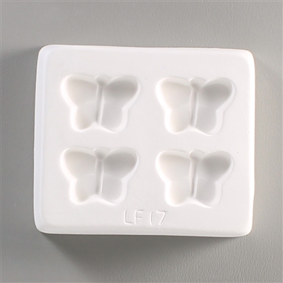 A square white ceramic mold for fusing hot glass on a grey background. Four identical small and simple butterflies have been carved into it with equal space between them. The mold says LF17 at the bottom.