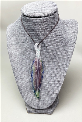 A grey fabric bust displays a fused glass feather pendant strung on a dark leather cord. The feather is shades of purple, blue, and green, and the base where it is strung is clear and iridescent.