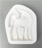 A pentagonal white ceramic mold for fusing hot glass on a grey background. A profile of a standing has been carved into it. The unicornâ€™s head is turned back to look left though its body is facing right, and its tail is slightly raised.