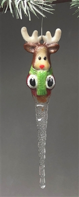 A fused glass reindeer ornament hanging from a pine branch on a grey background. The reindeer is brown with a tan face and antlers and a red nose. It is wearing a green scarf, and its body tapers into a clear icicle.
