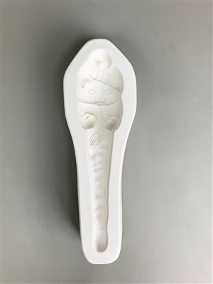 A long white ceramic mold for fusing hot glass on a grey background. A cat in a knit cap, scarf, and mittens and a body tapering into an icicle has been carved into it. The hat has a post in it allowing for hanging after firing.