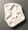 A white ceramic mold for fusing hot glass on a grey background. A top-down view of a large frog has been carved into it. The frog is plain in design and facing slightly to the right. Its arms are bent around either side of its head and its legs are bent.