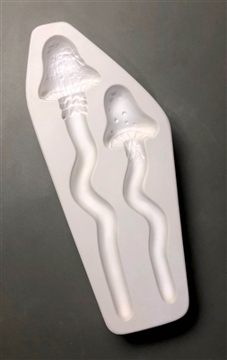 A roughly rectangular white ceramic mold for fusing hot glass on a grey background. Two different mushrooms with stems that elongate into wavy garden stakes have been carved into it. The left stake is slightly taller than the right.