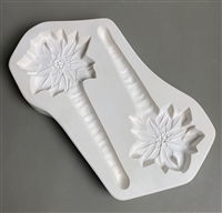 A white ceramic mold for fusing hot glass on a grey background. Two flat poinsettia flowers on top of thin stakes shaped like icicles have been carved into it. Each poinsettia has a post at its top to allow for hanging after fusing.