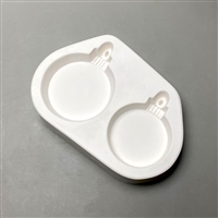 A white ceramic mold for fusing hot glass on a grey background. Two plain round ornaments have been carved into it. The left ornament is slightly larger than the right. Each ornament has a top with a post allowing for hanging after fusing.