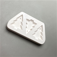 A white ceramic mold for fusing hot glass on a grey background. Three plain Christmas tree shapes have been carved into it. The middle tree is inverted compared to the two trees on its sides, but all are identical. Each has a post at the top.