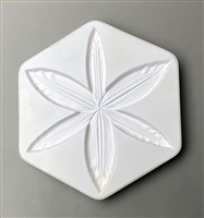 A hexagonal white ceramic mold for fusing hot glass on a grey background. A detailed flat lily flower has been carved into it. The lily has six petals, and the very edge of each petal has a slight ripple like a real lily.