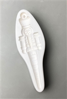 A long white ceramic mold for fusing hot glass on a grey background. A detailed nutcracker with legs tapering into an icicle has been carved into it. There is a post at the top of the nutcrackerâ€™s hat for hanging after firing.