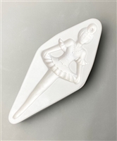 A diamond-shaped white ceramic mold for fusing hot glass on a grey background. A ballerina with legs tapering into an icicle has been carved into it. Her hands extend to the edges of her tutu. There is a post in her hair bun allowing for hanging.