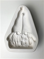 A triangular white ceramic mold for fusing hot glass on a grey background. Two gnomes leaning together have been carved into it. The left gnome has a beard and the right has pigtails. There is a post at top of their two hats to allow for hanging.