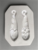 A rectangular white ceramic mold for fusing hot glass on a grey background. Two separate gnome faces have been carved into it. Both gnomes have tall hats with posts at the top for hanging. The left mold has a beard and the right has pigtails.