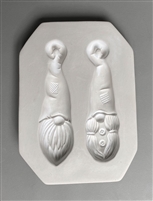 A rectangular white ceramic mold for fusing hot glass on a grey background. Two separate gnome faces have been carved into it. Both gnomes have tall hats with posts at the top for hanging. The left mold has a beard and the right has pigtails.