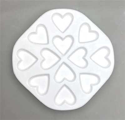 An octagonal white ceramic mold for fusing hot glass on a grey background. Twelve identical plain hearts have been carved into it. The hearts are evenly spaced apart radiating out from the center.