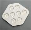 A hexagonal white ceramic mold for fusing hot glass on a grey background. Eight identical paw prints have been carved into it. There is equal space around each paw, and their placement is mirrored on each side of the mold.