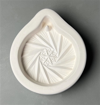 A white ceramic mold for fusing hot glass on a grey background. A detailed round ornament with a faceted crystal pattern has been carved into it. The top of the ornament has a post to allow for hanging after fusing.