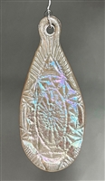 A tear-shaped, fused glass Christmas ornament hanging in front of a grey background. The ornament has an intricate cut crystal design, and is made from iridescent, cream-colored glass.