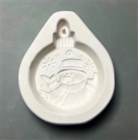 A white ceramic mold for fusing hot glass on a grey background. A round ornament with a smiling snowman design has been carved into it. The snowman has a top hat, mittens, and scarf, and is positioned with his arms up. He is surrounded by snowflakes.