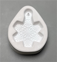 A white ceramic mold for fusing hot glass on a grey background. A large six-armed snowflake with an intricate cut crystal has been carved into it. The top of the snowflake has a post to allow for hanging after fusing.
