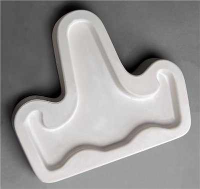 A T-shaped white ceramic mold for fusing hot glass on a grey background. A simple flat easel shape with a long back part and two slightly curved arms on either side has been carved into it.