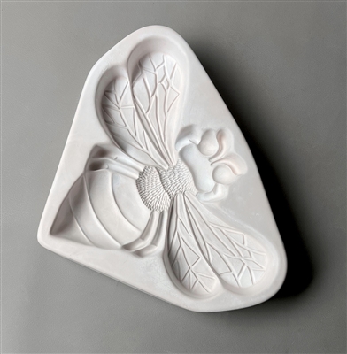 A triangular white ceramic mold for fusing glass displayed on a grey background. A large and very detailed top-down view of a bumblebee has been carved into it.