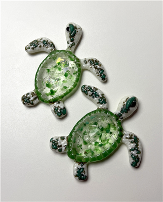 Two small turtles made from fused glass. Their fins and heads are cream with speckles of teal all along them. Their shells are ringed in opaque green and filled in with clear glass with flecks of various greens inside it as well.