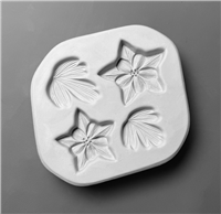 A white ceramic mold for fusing glass in the shape of a somewhat rounded square. Two flowers and two leaves are carved into it, all very detailed. The flowers resemble columbine flowers, with five outer and five inner petals.
