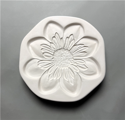 An octagonal white ceramic mold for fusing glass on a grey background. A flower with eight large teardrop shaped outer petals, a complex arrangement of smaller inner petals, and a large, circular center has been carved into it.