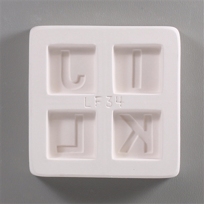 A square white ceramic mold for fusing hot glass on a grey background. Four separate but identically sized squares have been carved into it with equal space between them. Each square has one of the letters I, J, K, or L carved in block print in it.